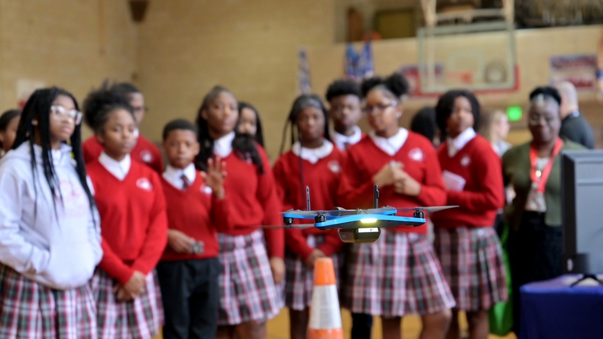 Students watch a drone taking off from the floor.