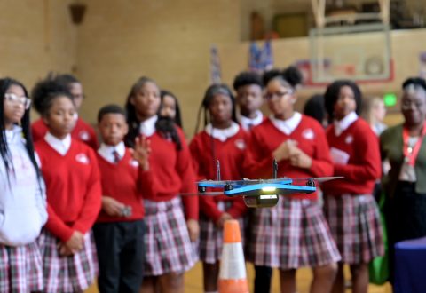Students watch a drone taking off from the floor.
